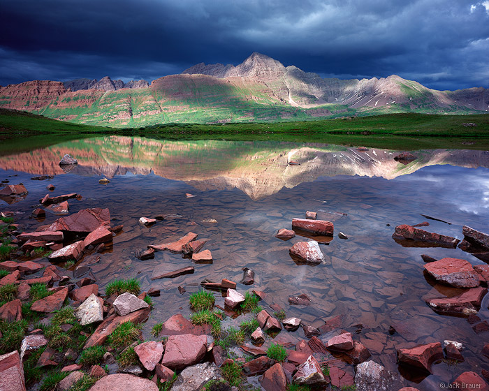 Afternoon sunlight beams on the Maroon Bells fourteeners, as seen from high in Fravert Basin - July. The dark storm clouds were...